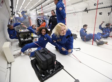 Forskere i kjeledresser holder seg fast i flyet under en parabolsk flyvning.